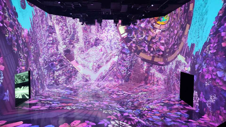 Purple and cyan immersive projections extending across the walls and floor at ARTECHOUSE.